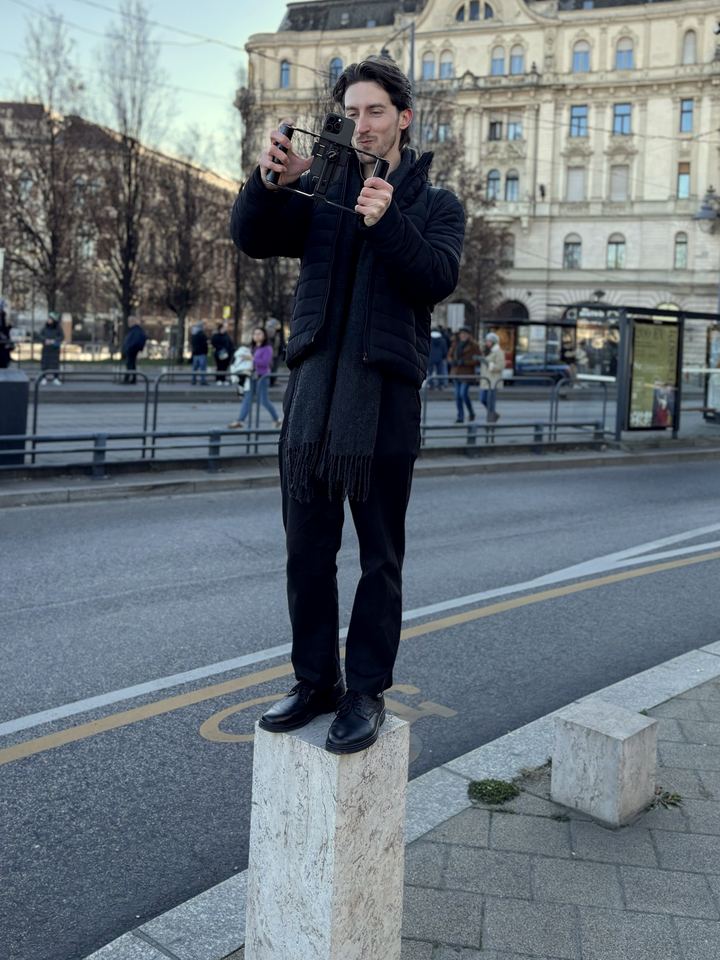 Tálas Levente egy kőoszlopon állva forgat telefonnal Budapesten